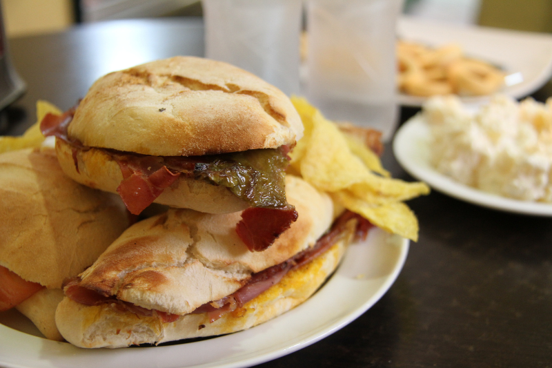 Sandwiches with chips on a plate and blurred food in the background.